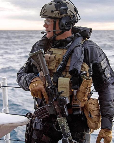 Soldat en tenue tactique avec un fusil sur fond de mer.