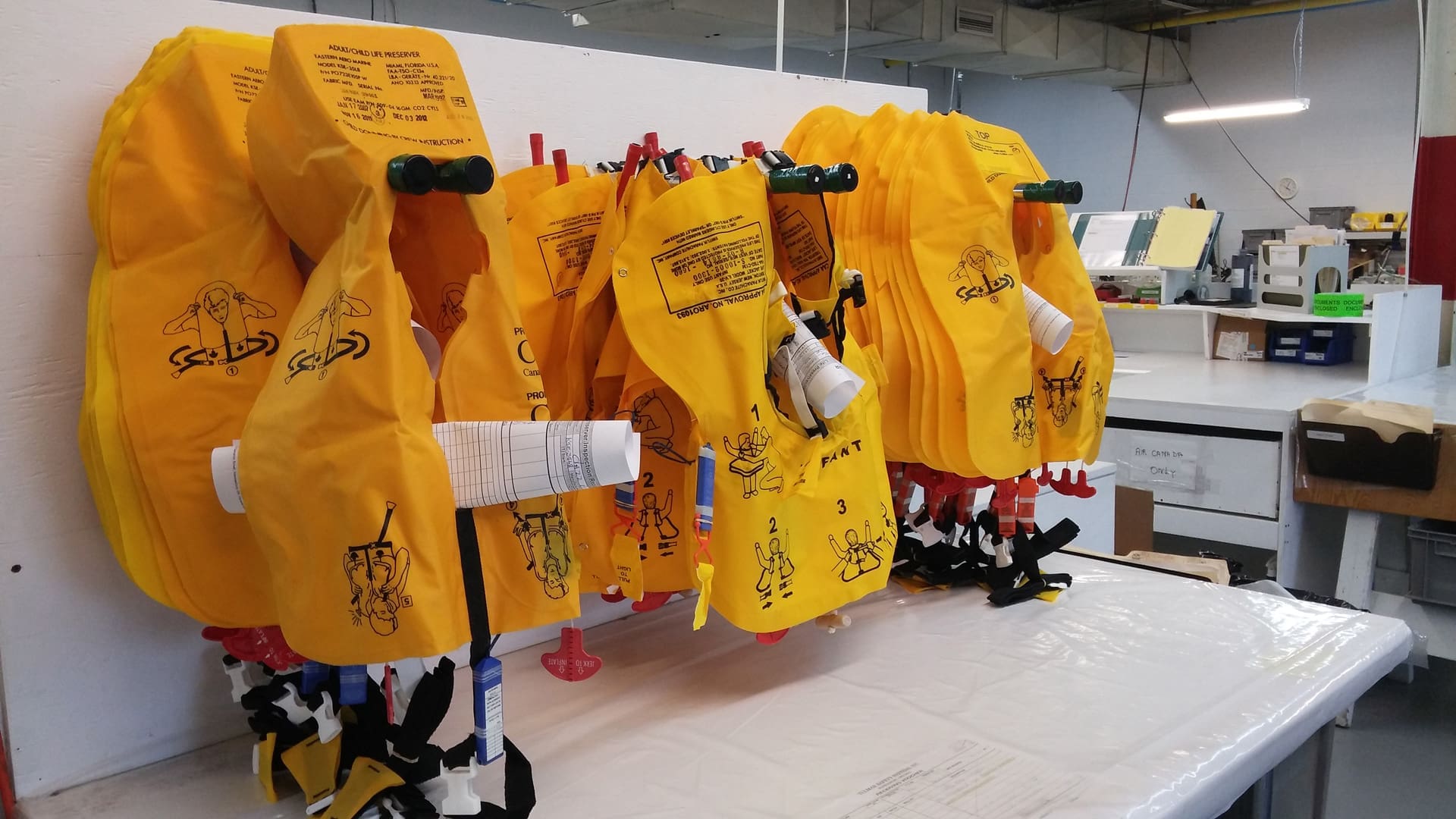 Des gilets de sauvetage jaunes sont suspendus dans un atelier, avec des illustrations et un texte sur les instructions d'utilisation.