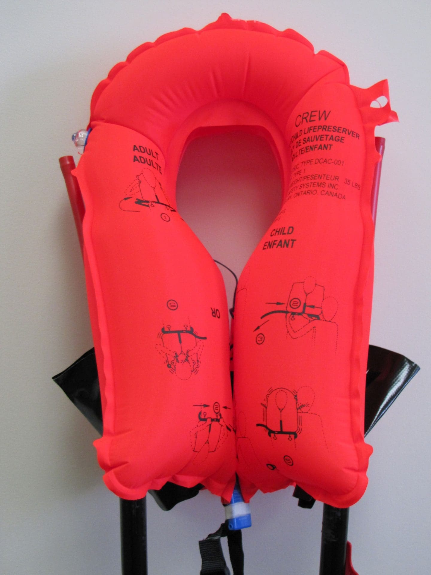 Gilet de sauvetage pour adulte rouge vif avec des images d'instruction, accroché à un mur blanc.
