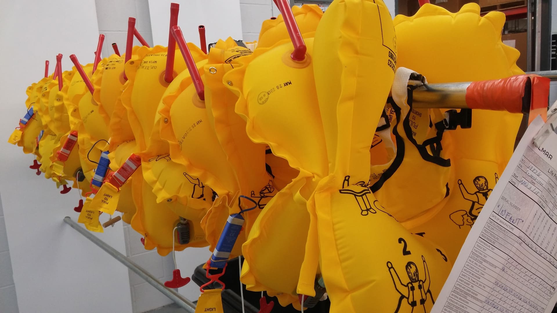 Rangée de gilets de sauvetage jaunes gonflés suspendus à un support.